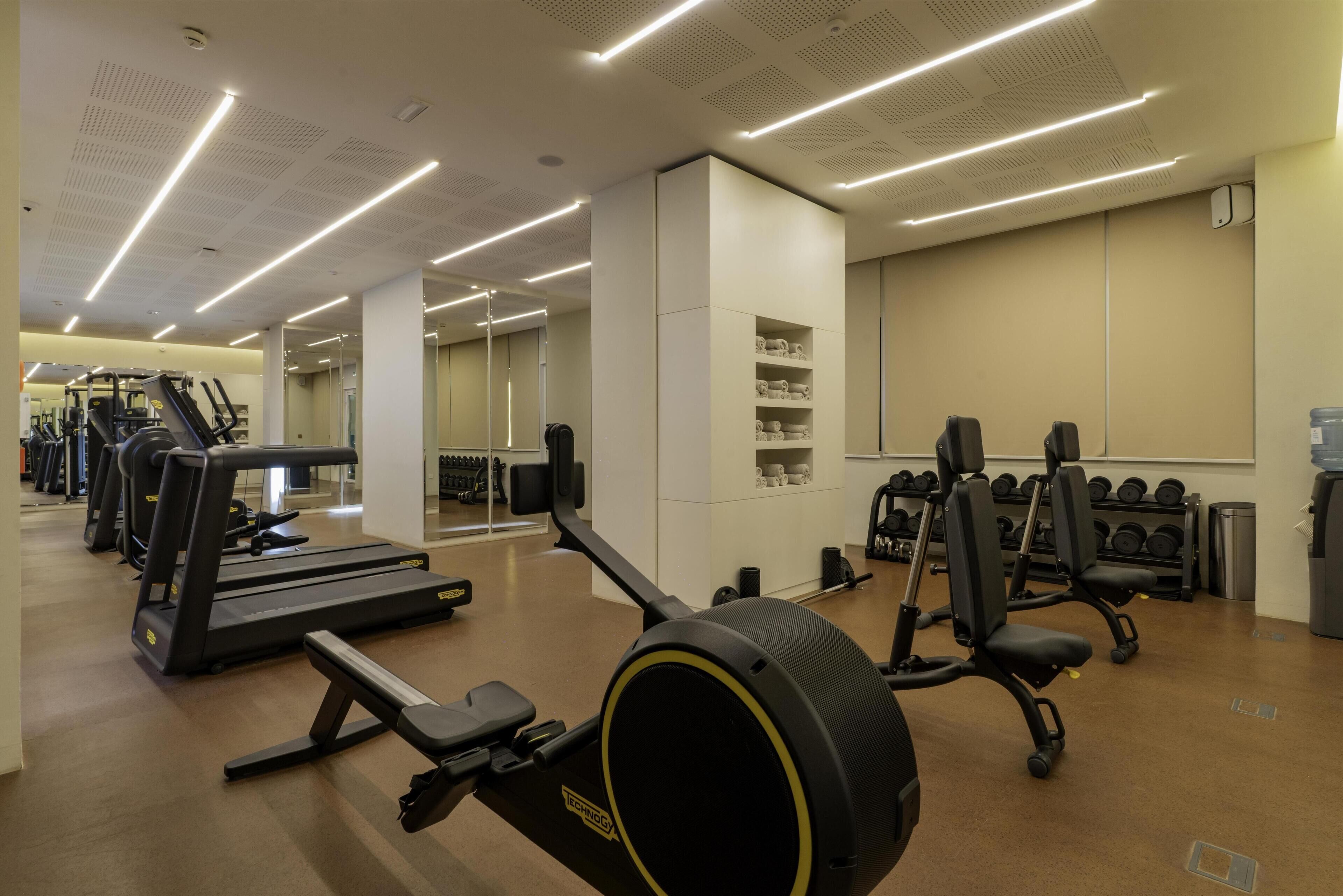 A gym with cardio machines, weight benches, and dumbbells.