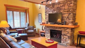 Una sala de estar con chimenea de piedra, sofás de cuero, televisor y repisa de la chimenea.