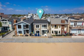 A beachfront residential area with modern houses, a sandy beach, and a clear blue sky. - Giant Beachfront Home with Parking near the Pier (Newport Beach)