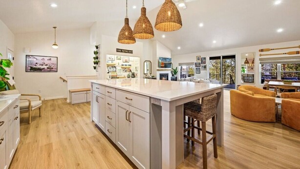 A modern kitchen with a central island, pendant lighting, and a dining area with a view.