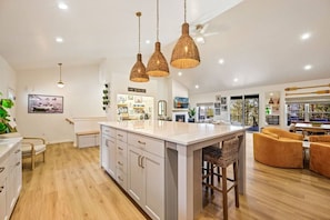 A modern kitchen with a central island, pendant lighting, and a dining area with a view.