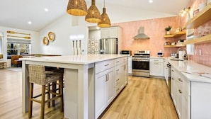 A modern kitchen with a central island, white cabinetry, stainless steel appliances, and wicker pendant lighting.
