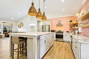 Una cucina moderna con isola centrale, mobili bianchi, elettrodomestici in acciaio inossidabile e lampade a sospensione in vimini.