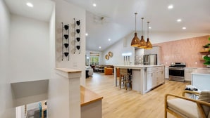 A modern kitchen with a central island, pendant lighting, and a dining area with a wooden table and chairs.
