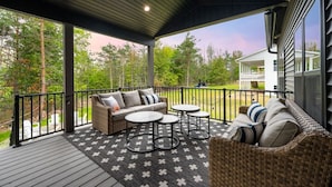 A covered outdoor seating area with a sofa, two round tables, and a wicker chair.