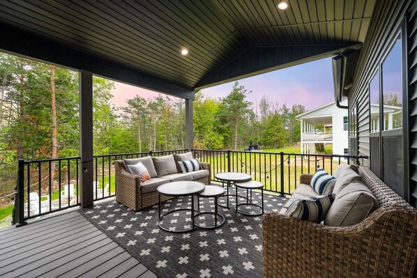 A covered outdoor seating area with a sofa, two round tables, and a wicker chair.