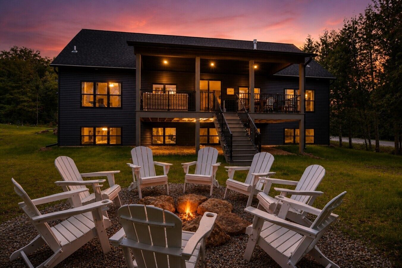 A two-story house with a fire pit and Adirondack chairs in the front yard.