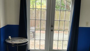 A room with a sliding glass door leading to an outdoor patio, a small round table, and a green doormat. - Duplex Back Apartment (Vero Beach)