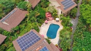 A residential area with multiple houses, each equipped with solar panels on the roofs. There is a swimming pool in the center surrounded by greenery. - Peaceful Retreat • 5 min Walk to Town, Pier & Beach • Free Parking (Kailua-Kona)