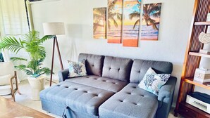 A living room with a grey sectional sofa, a potted plant, and a bookshelf. - Peaceful Retreat • 5 min Walk to Town, Pier & Beach • Free Parking (Kailua-Kona)