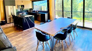 A spacious kitchen with modern appliances, a dining area with a large table and chairs, and large windows offering a view of the outdoors. - Timberwolf A Cabin at Sasquatch Mountain  *HOT TUB* GAMES ROOM* (Agassiz)