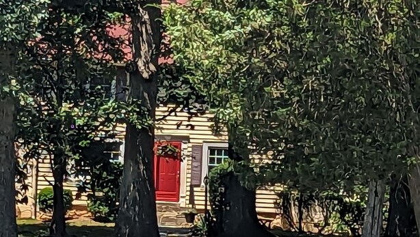 Un bâtiment avec une porte rouge, entouré d’arbres et d’herbe.
