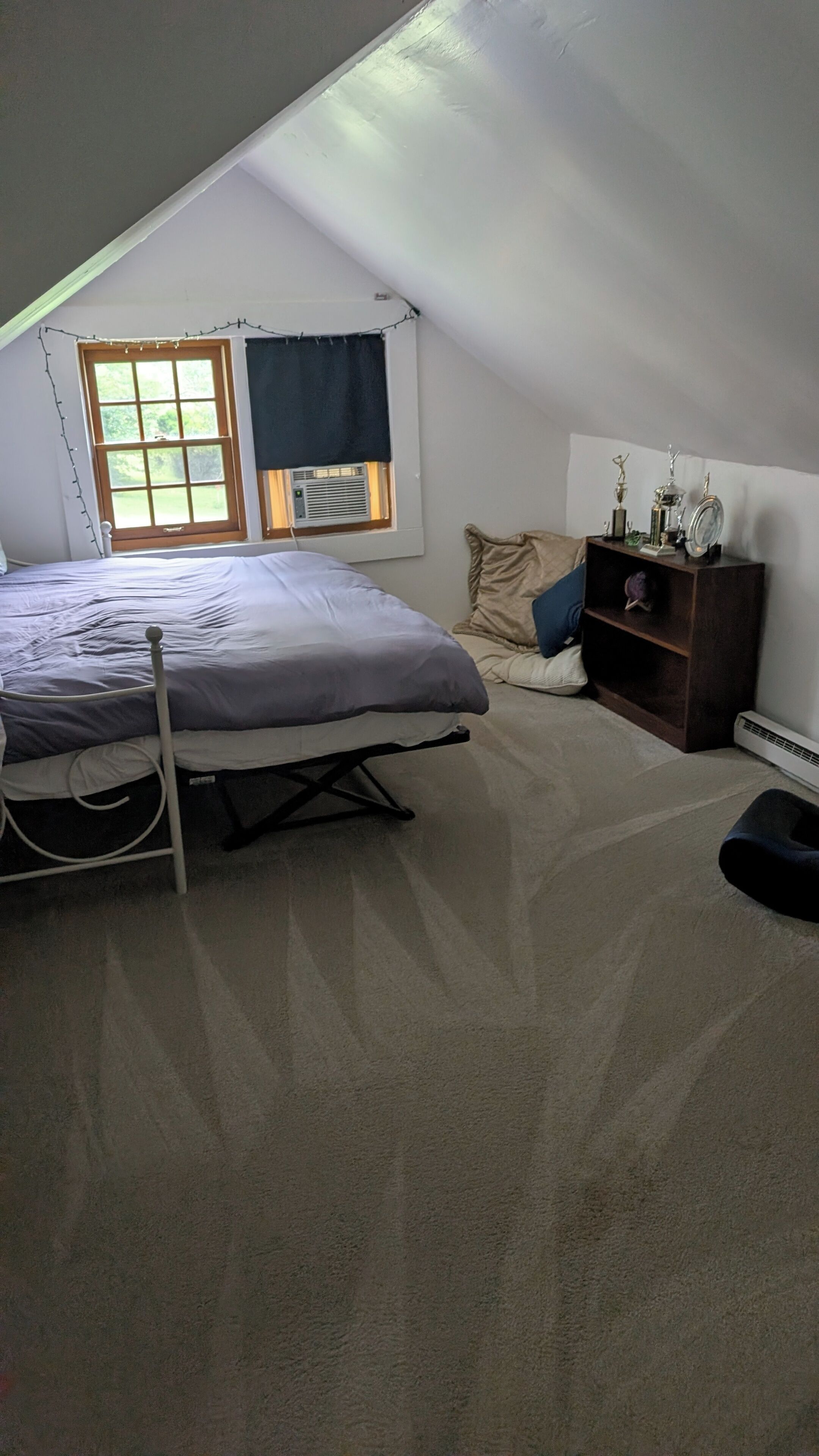 Une chambre à coucher avec un lit, une fenêtre avec des rideaux, un radiateur et une étagère où sont exposés des trophées.