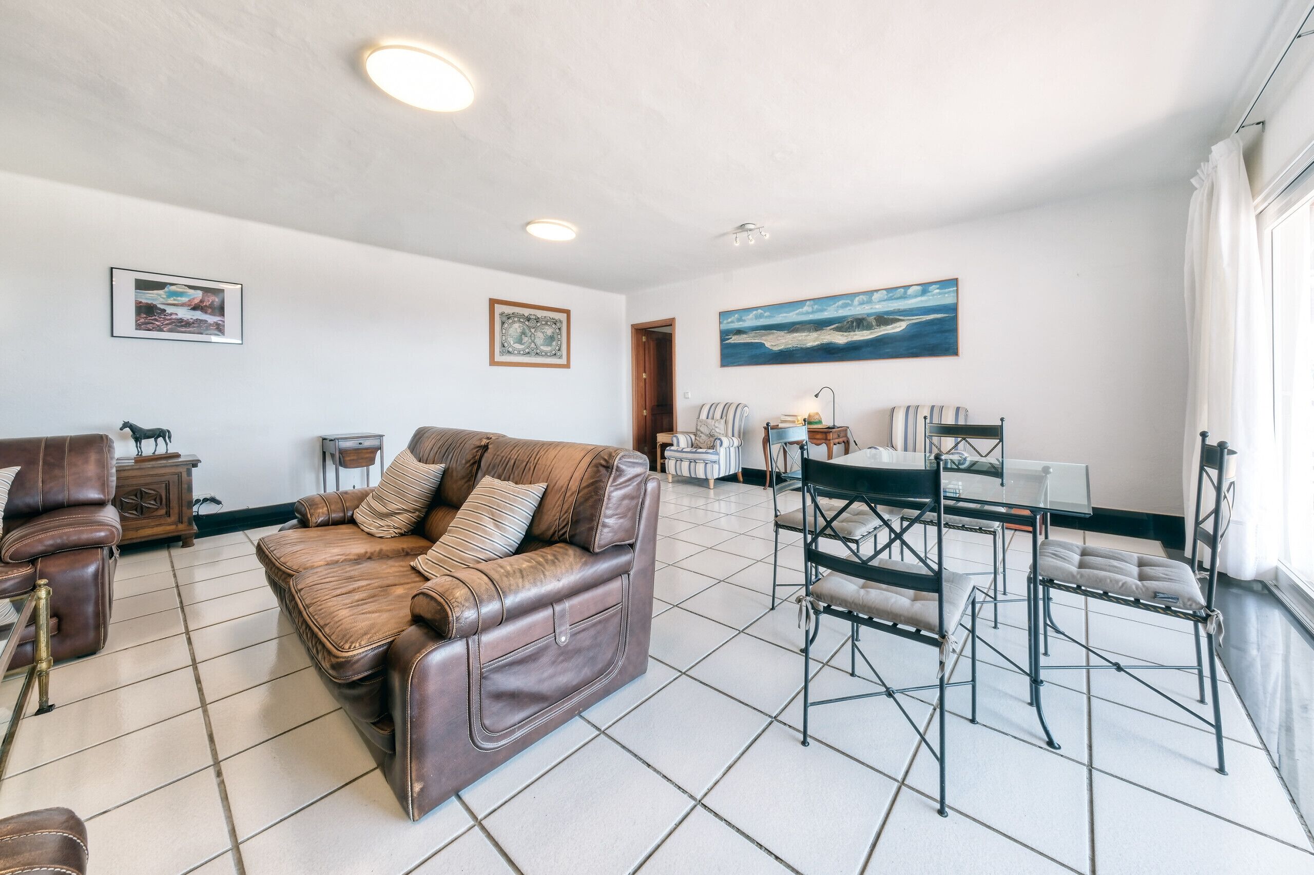 Ein Wohnzimmer mit braunem Ledersofa, einem Esstisch mit Stühlen und einem Gemälde an der Wand.