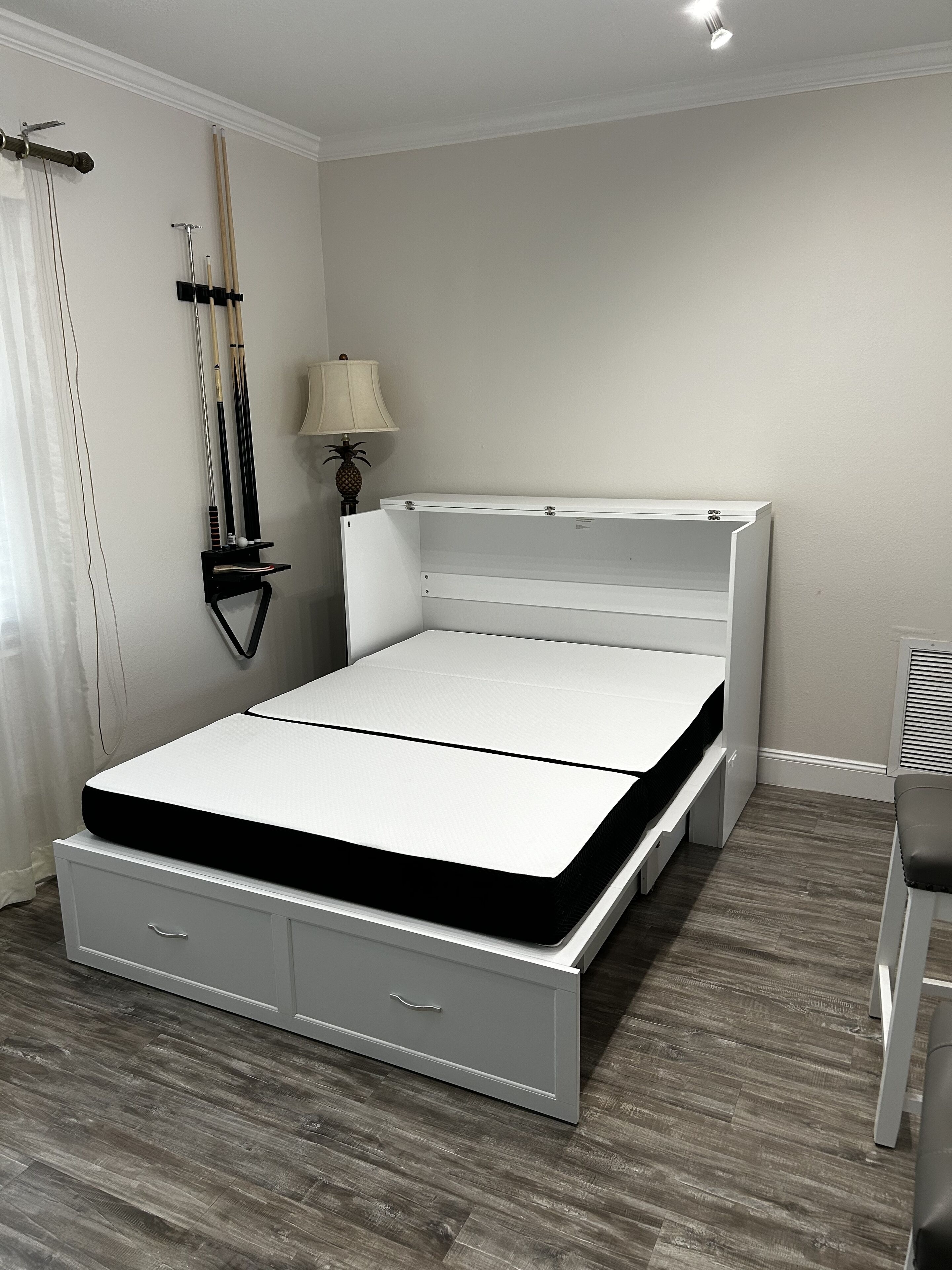 Een keurig opgemaakt slaapkamer met een bed, nachtkastje, lamp en een wandrek met sportartikelen.