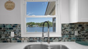 Une cuisine avec une fenêtre donnant sur un lac, un évier et un crédence décorée de carreaux bleus et blancs.