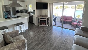A modern living room with a large ceiling fan, a kitchen area with a built-in microwave, and a sliding glass door leading to an outdoor patio. - Welcome to the scallop shack! Newly renovated and on the water in Crystal River! (Crystal River)