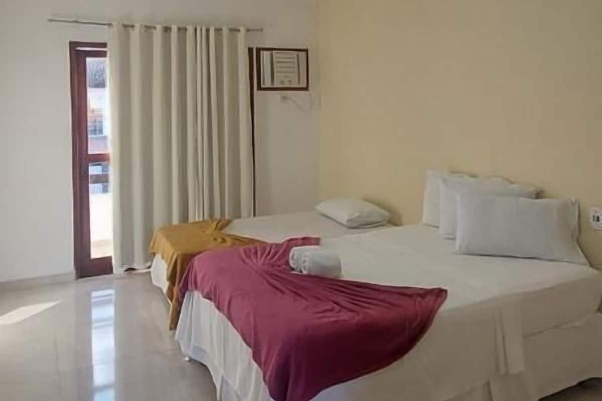 A hotel room with two beds, a large window with curtains, a door, and a ceiling light.