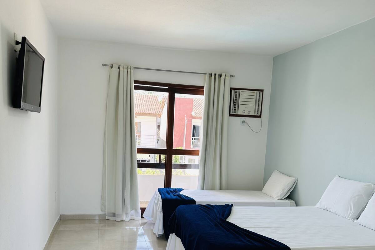 A hotel room with two beds, a TV mounted on the wall, and a window with curtains.