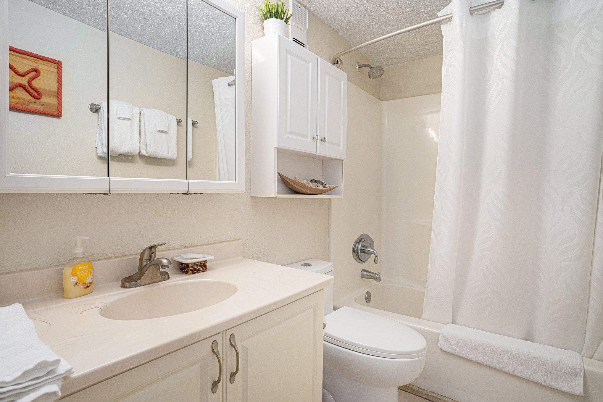 Baño con lavabo, inodoro y ducha. Hay armarios blancos sobre el lavabo y un perchero con toallas.