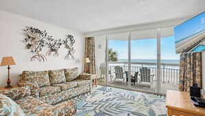 A living room with a sofa, a coffee table, a TV, and a balcony with a view of the beach. - Oceanfront 2bed/2bath-Water's Edge Resort-111 Indoor/Outdoor Pool & Hot Tub (Garden City Beach)