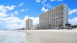 A beachfront hotel with multiple floors, a sandy beach, and palm trees. - Oceanfront 2bed/2bath-Water's Edge Resort-111 Indoor/Outdoor Pool & Hot Tub (Garden City Beach)
