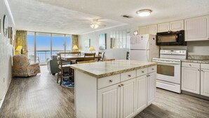 Una cocina amplia con armarios blancos, una isla central, un comedor con mesa y sillas, y vistas a través de grandes ventanales.
