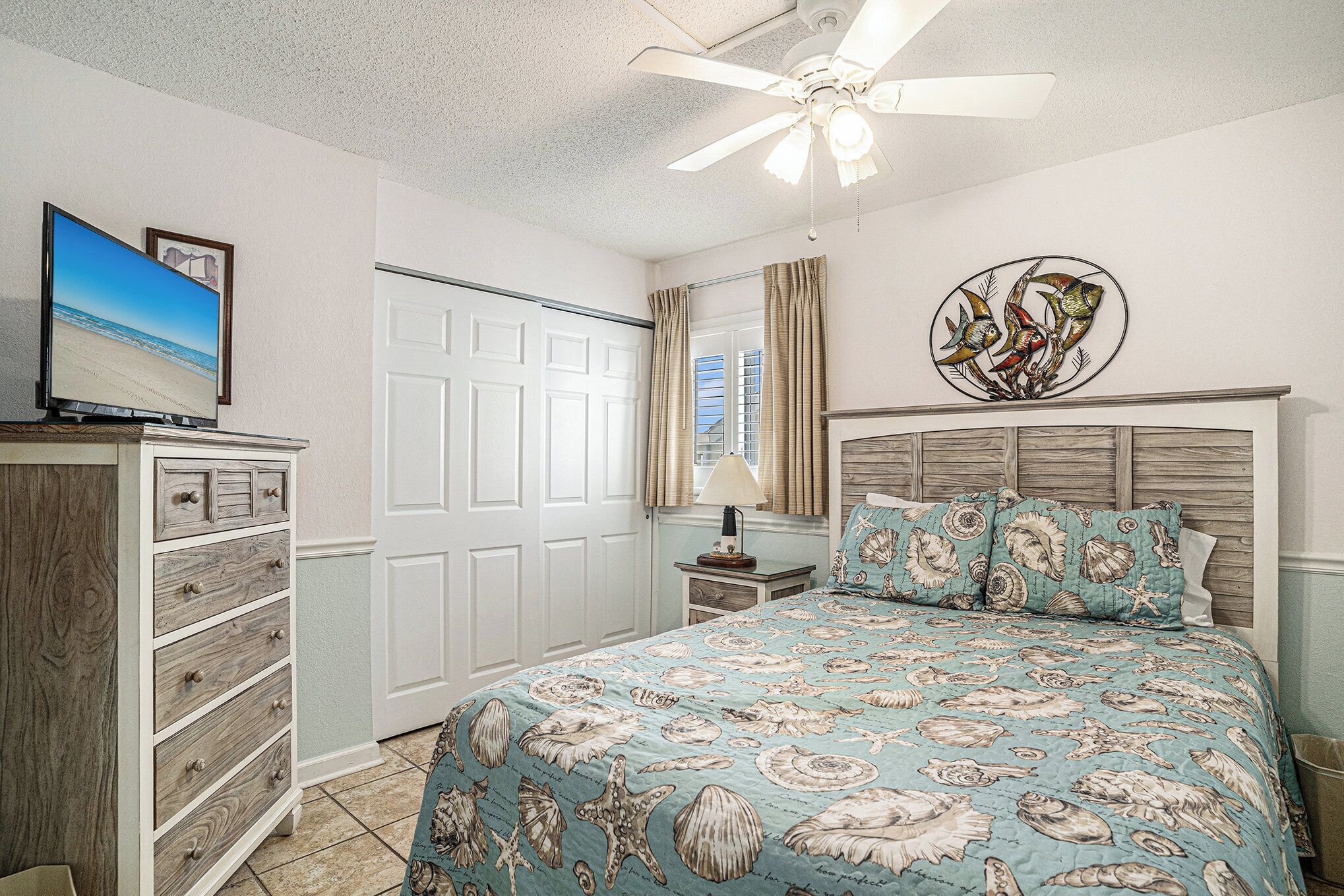 A bedroom with a bed, dresser, ceiling fan, and artwork on the wall.