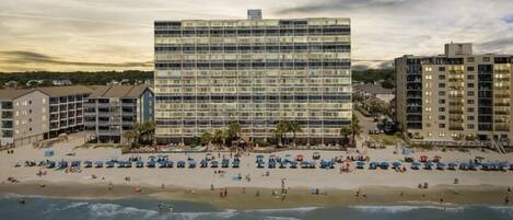 Un hotel frente a la playa con varios pisos, una zona de piscina y vistas al mar.