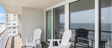 Ein Balkon mit weißen Adirondack-Stühlen, einem runden Tisch und Blick aufs Meer.
