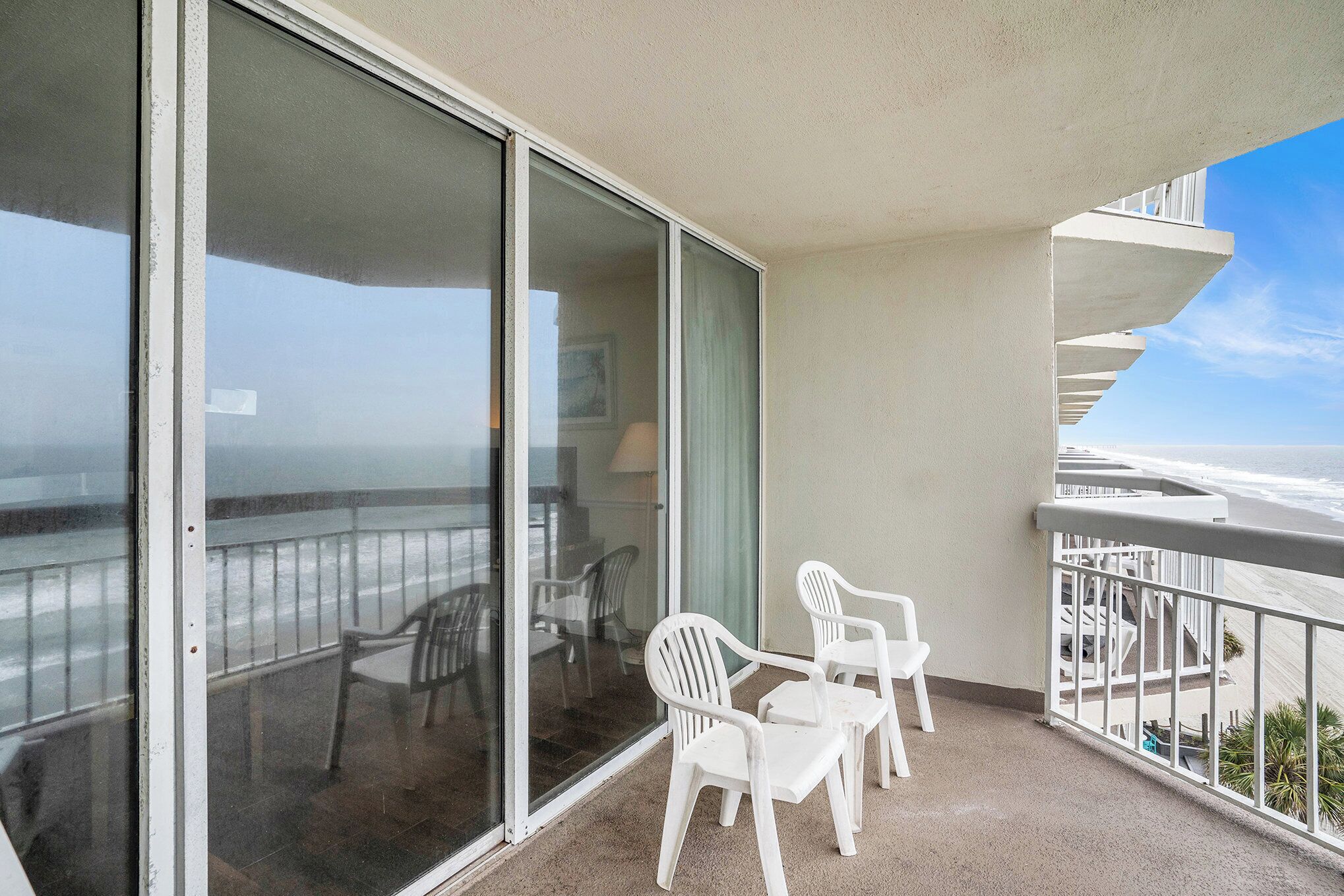 A balcony with a view of the ocean, white plastic chairs, and a glass door.