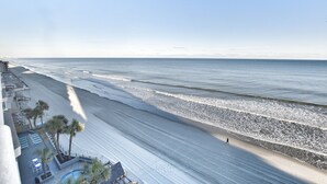 A beach view with a long stretch of sand, a few palm trees, and a person walking. - Oceanfront 2bed/2bath-Water's Edge Resort-711 Indoor/Outdoor Pool & Hot Tub (Garden City Beach)