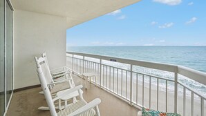 Een balkon met witte rieten stoelen en een tafeltje, met uitzicht op een strand met een 'NO PARKING' bord.