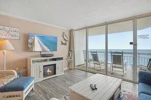 A living room with a fireplace, a television, and a view of the ocean through a sliding glass door.