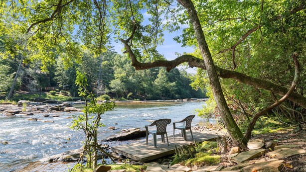Una terrazza sul fiume con sedie, circondata da rocce e vegetazione.