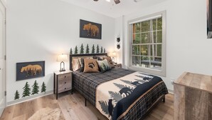 Camera da letto con un letto, un comodino, una ventola a soffitto, una finestra con persiane e decorazioni murali tra cui un orso e alberi.