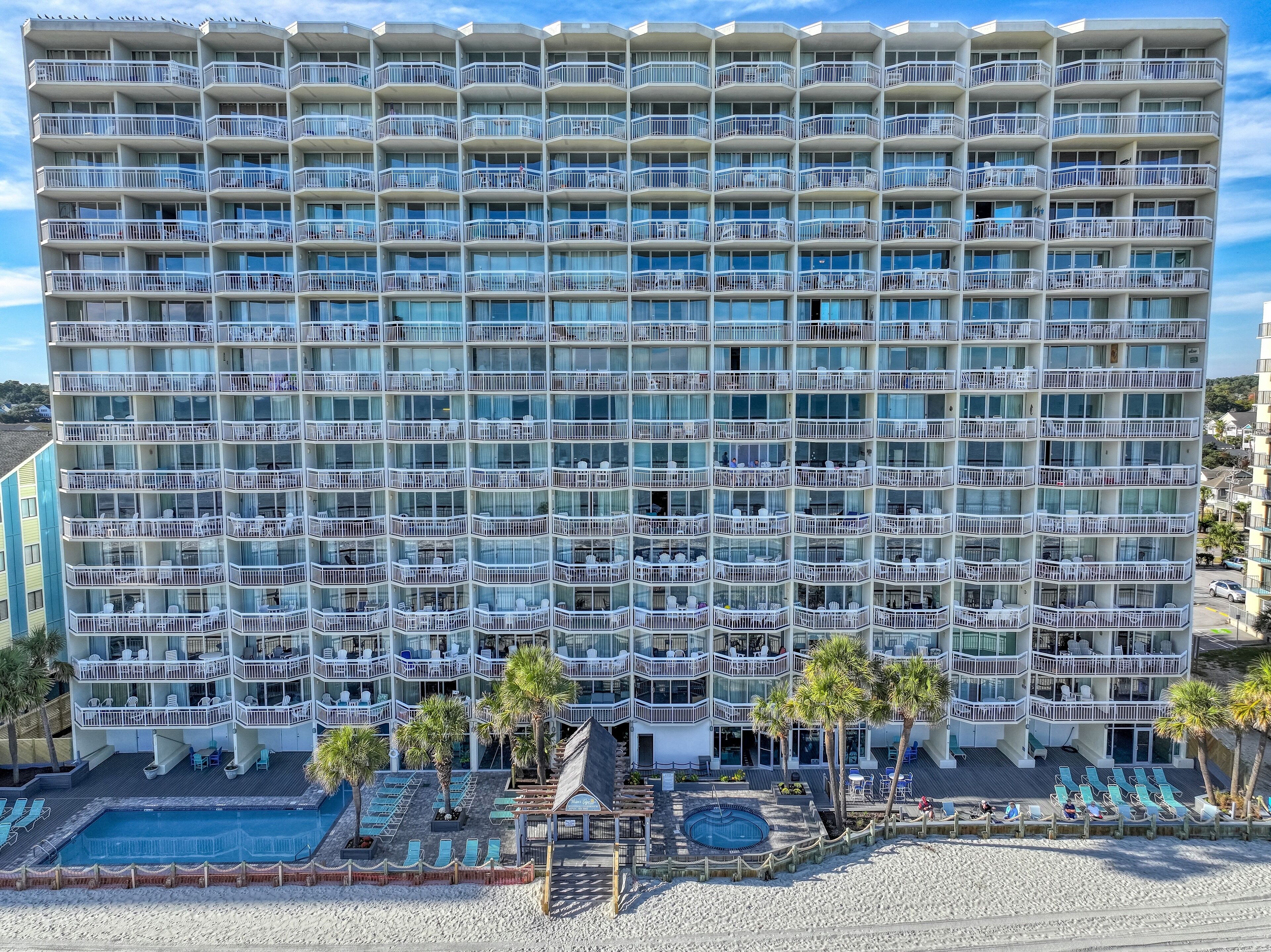 A multi-story hotel with balconies, a pool area, and palm trees.