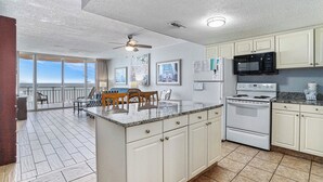 A kitchen with a large island, white cabinets, a microwave, stove, and a view of the ocean through large windows. - Oceanfront 1bed/2bath-Water's Edge Resort-1206 Indoor/Outdoor Pool & Hot Tub (Garden City Beach)