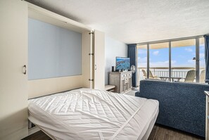 Una habitación de hotel con cama, zona de estar, televisión y vista al mar.