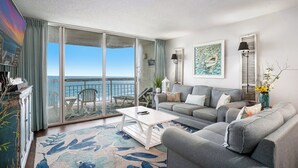 A spacious living room with a large sliding glass door leading to a balcony with a view of the sea. - Oceanfront 2bed/2bath-Water's Edge Resort-602 Indoor/Outdoor Pool & Hot Tub (Garden City Beach)