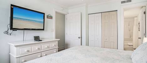 A bedroom with a bed, a TV on a dresser, a ceiling fan, and white doors.