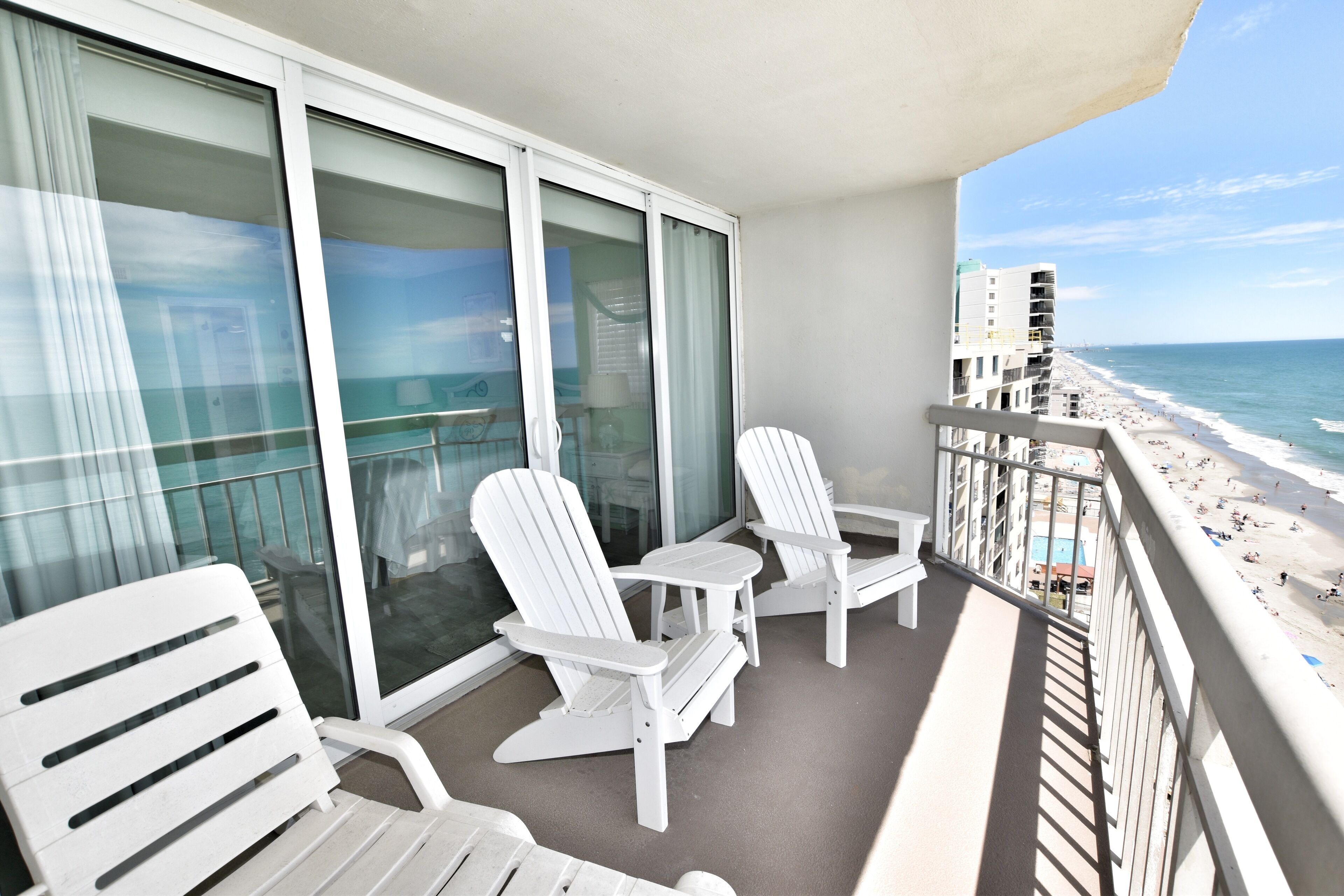 Een balkon met witte stoelen en een tafel, met uitzicht op een strand en de oceaan.