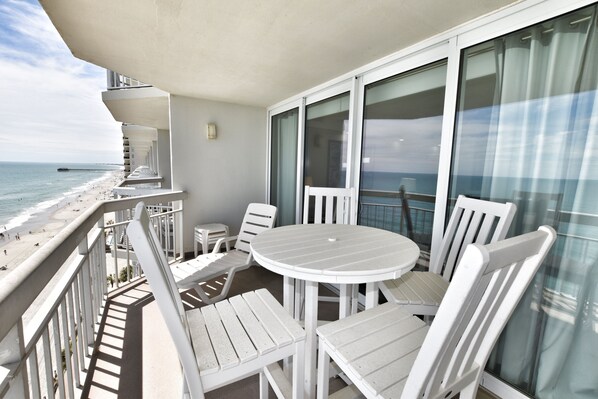 A balcony with a white table and chairs, overlooking a beach and ocean. - Oceanfront 3bed/2.5bath-Water's Edge Resort1001 Indoor/Outdoor Pool & Hot Tub (Garden City Beach)