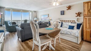 A room with a dining table, chairs, a sofa, and a ceiling fan. - Oceanfront 1bed/2bath-Water's Edge Resort-1405 Indoor/Outdoor Pool & Hot Tub (Garden City Beach)