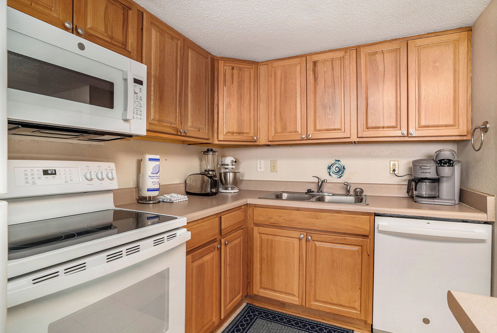 A compact kitchen with wooden cabinets, a microwave, a stove, a dishwasher, and a coffee maker.