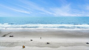 A beach with a clear sky, calm sea, and a few people and beach equipment. - Oceanfront 3bed/2.5bath-Water's Edge Resort-612 Indoor/Outdoor Pool & Hot Tub (Garden City Beach)