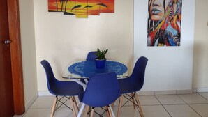 A dining area with a table, chairs, and a wall art piece depicting a sunset and dolphins. - Rua Maria Tognini 450 (Praia Grande)