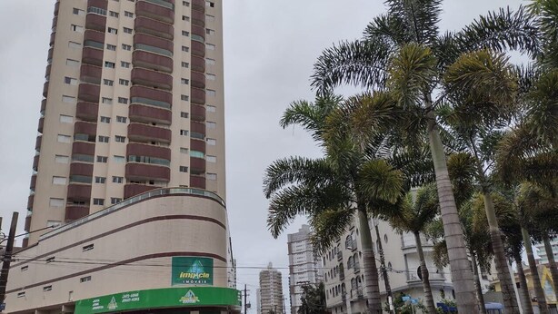 A tall building with a green sign for a moving company. - Rua Maria Tognini 450 (Praia Grande)