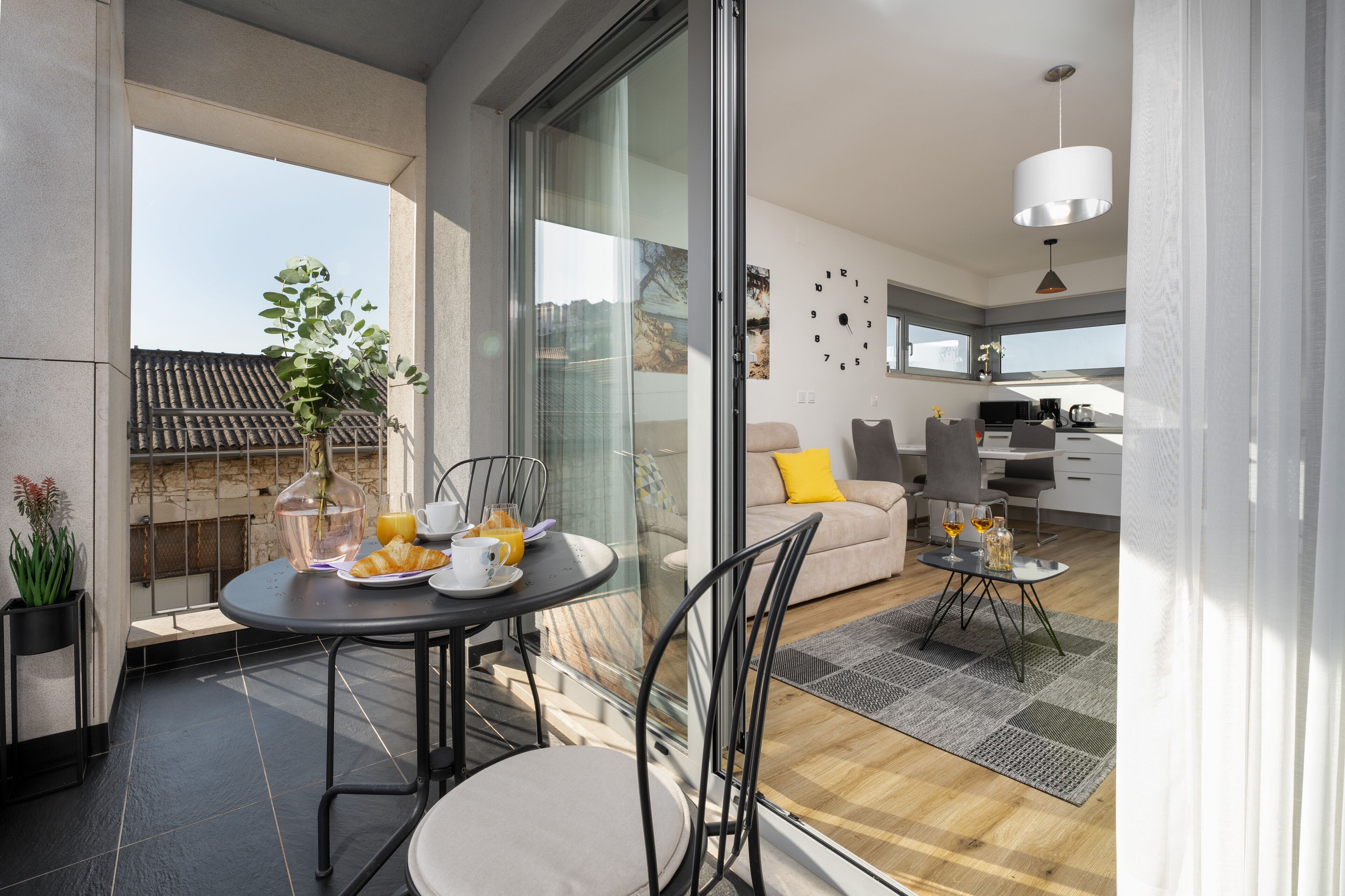 A modern living space with a balcony, a dining area with a table and chairs, a sofa, and a kitchen area.