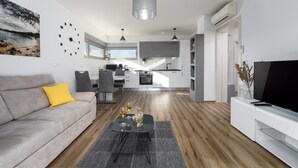 A modern living room with a sofa, coffee table, and a TV. There is a kitchen in the background with cabinets and a window. - Modern apartment directly at the marina Vrsar and 300m from the beach (Vrsar)
